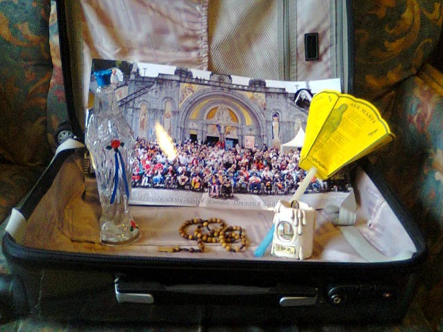 Valise ouverte contenant une Vierge de Lourdes, une bougie, un flambeau et une photo de groupe du pèlerinage de l'Hospitalité d'Evry